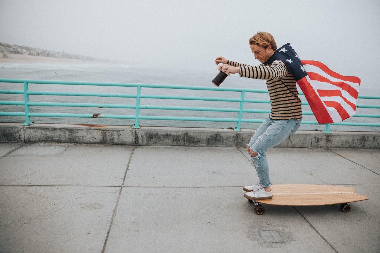 guy longboarding with the american flag as a cape