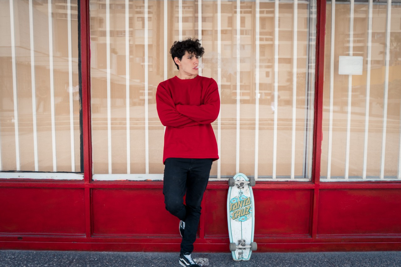 man leaning against store window with a penny board