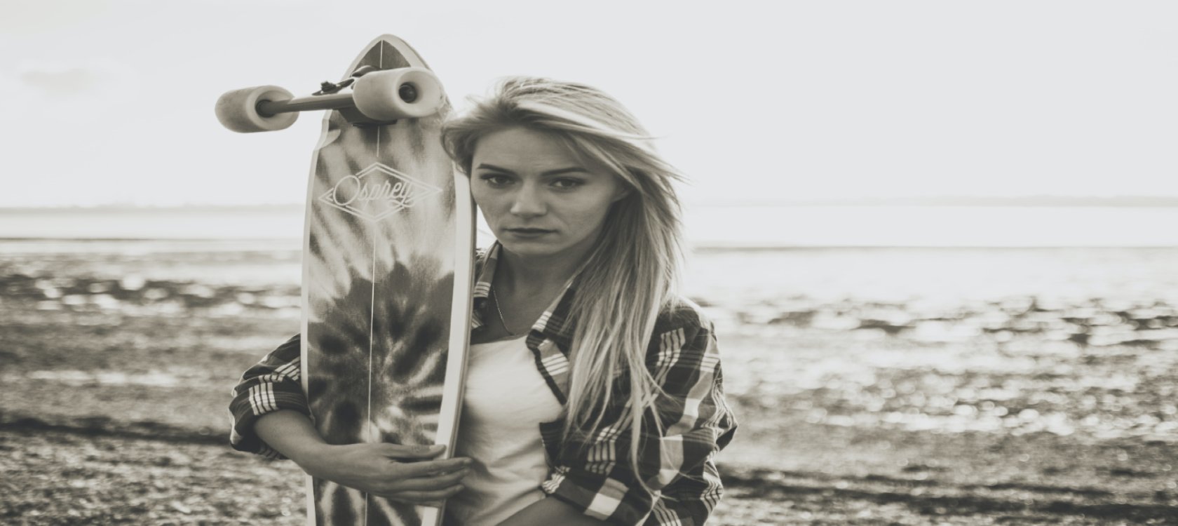Girl holds a longboard crusier infront of waves