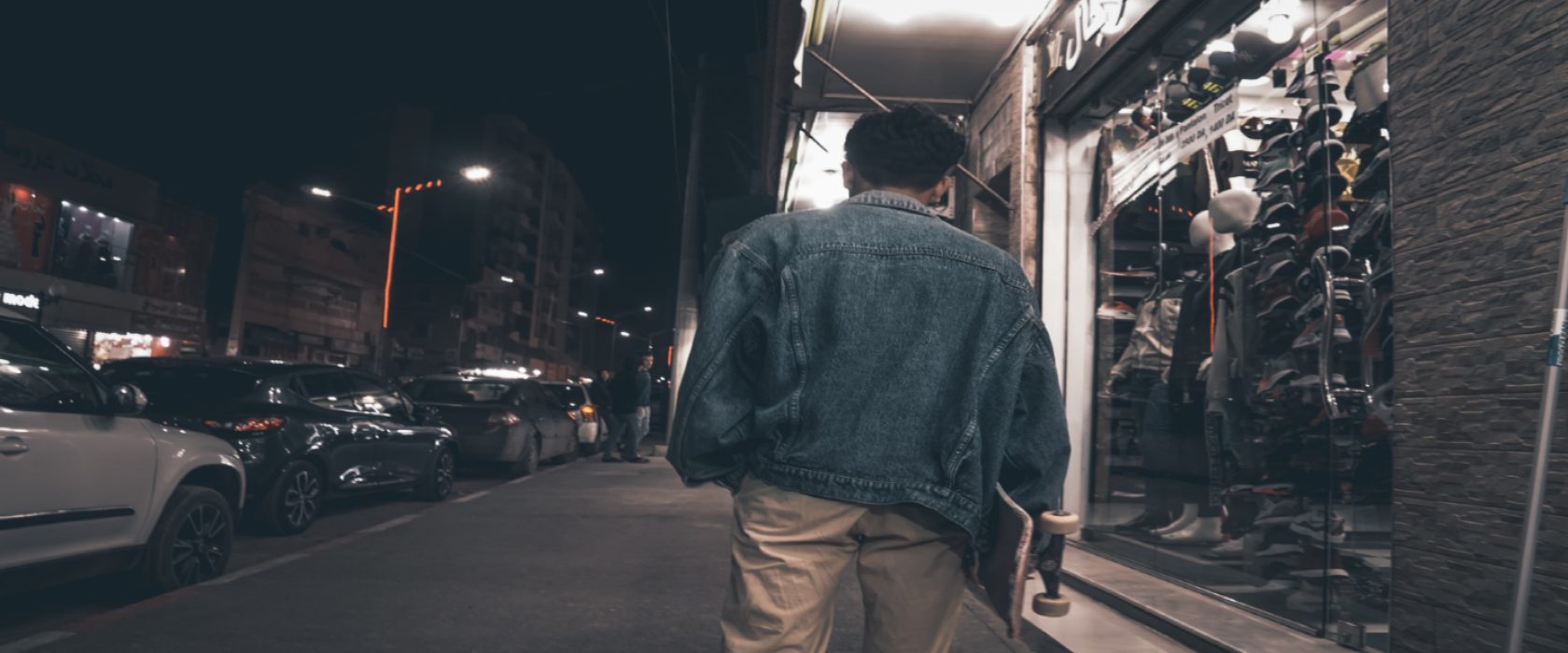 Guy holding a skateboard walking around at night